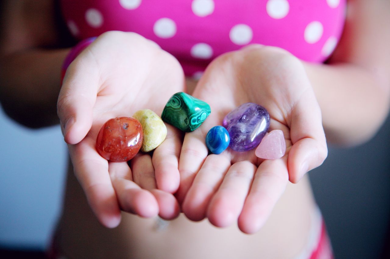 Vibrant selection of multicolor gemstones held in young woman's hands, featuring a variety of polished stones.